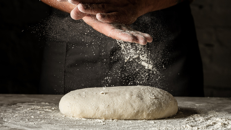 Hands covered in flour above bread dough