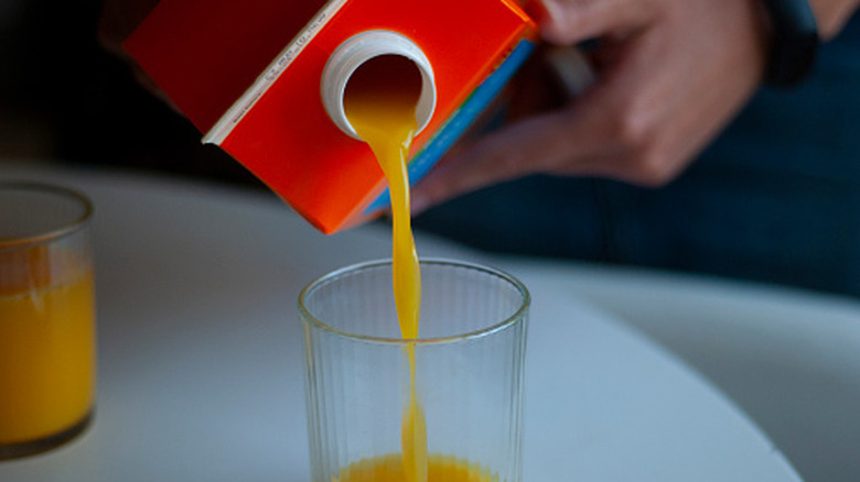 Someone pours a glass of orange juice from a carton