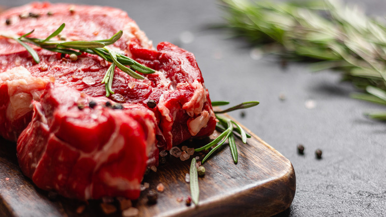A rock had a steak on a cutting board seasoned with some peppercorns, salt, and rosemary