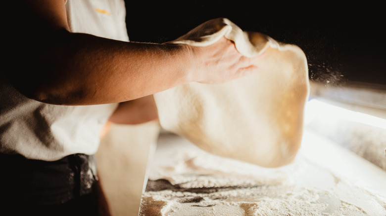 Person throwing pizza dough