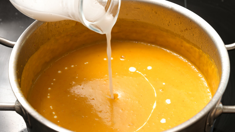 Coconut milk is poured into a pot of soup