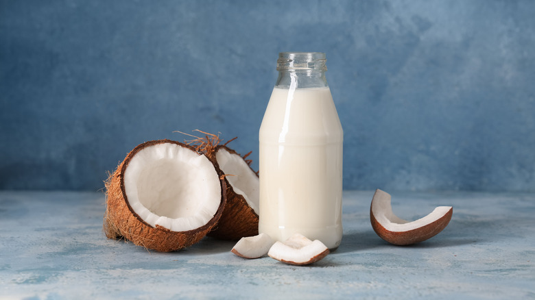 A jug of coconut milk surrounded by halved coconuts