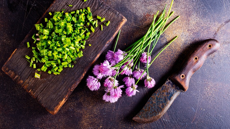 chive blossoms and chopped stems on a wooden cutting board with knife