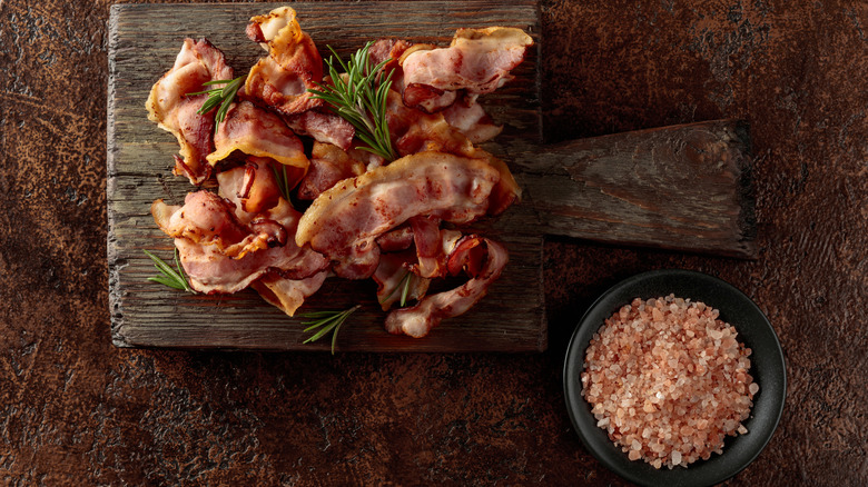 Cooked bacon on a wooden tray and a bowl of bacon seasoned salt