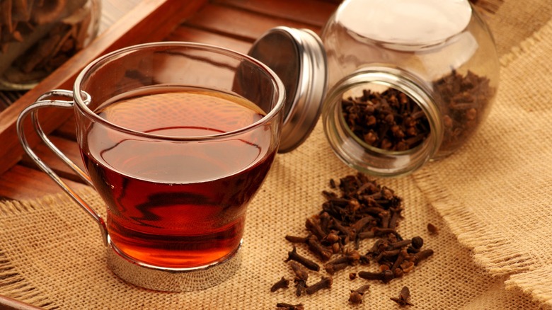 clove tea in a glass tea cup and whole cloves on a wooden tray