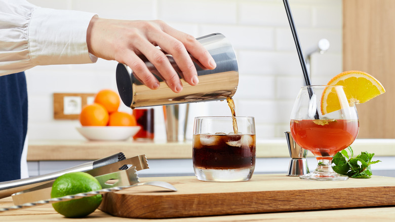 A person pours a homemade cocktail into a glass.