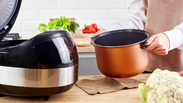 open slow cooker and person holding pot with cauliflower on side