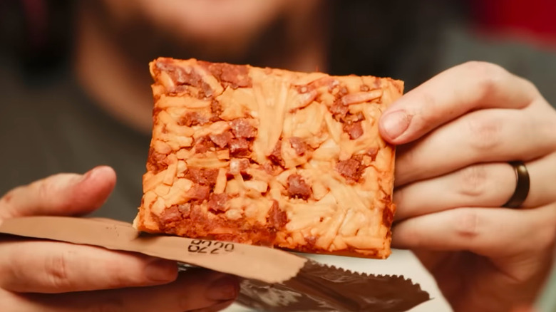 close up of a square slice of MRE pizza with pepperoni in hands