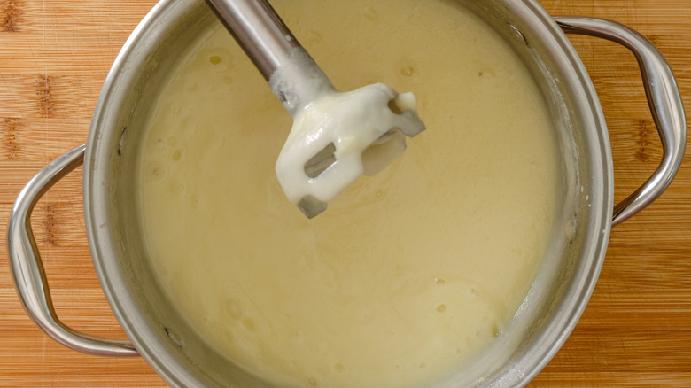 An immersion blender being used in a stock pot full of pale thick soup