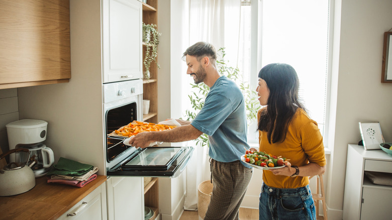 A couple placing a basket of French fries into the oven to air fry