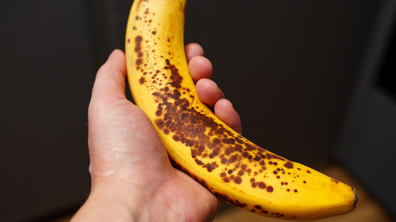 Ripe banana with brown spots being held