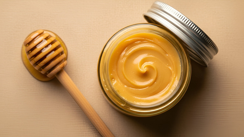 A jar of creamy honey with the lid off next to a honey wand coated in honey