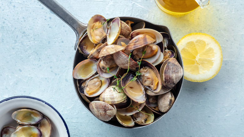 A skillet of cooked clams next to a half lemon