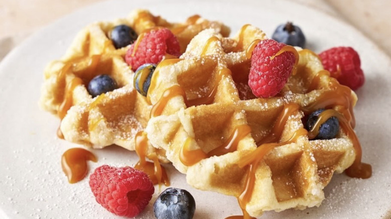 St. Pierre waffles topped with powdered sugar, berries, and caramel sauce