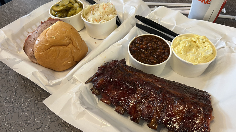 Two paper-lined trays with brisket sandwich, short ribs, and barbecue sides at Bogart's Smokehouse