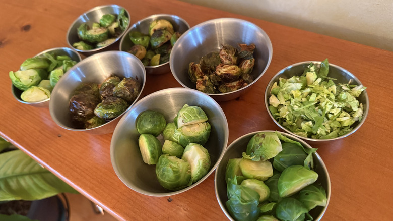 Eight stainless steel bowls with Brussels sprouts on wooden table