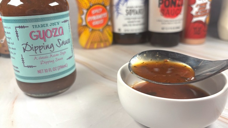 Spoon dipped into gyoza dipping sauce next to bottle, other sauces behind