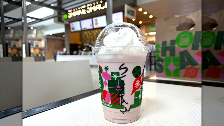 A light pink milkshake topped with whipped cream in a disposable cup