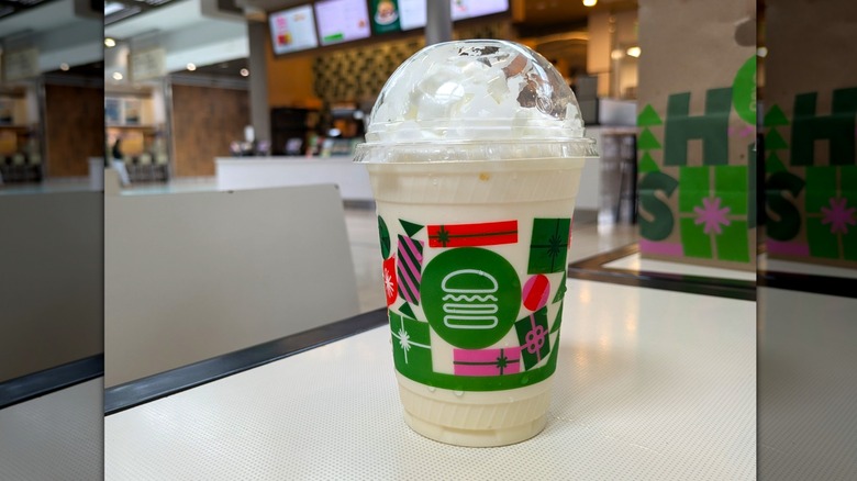 A creamy white vanilla milkshake topped with whipped cream in a disposable cup