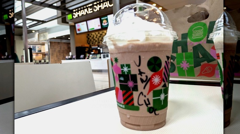 A milkshake with vanilla and chocolate custard combined is topped with whipped cream in a disposable cup.