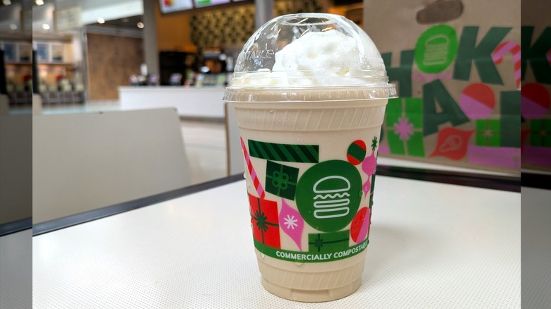 A light brown, almost tan, milkshake is in a disposable cup topped with whipped cream