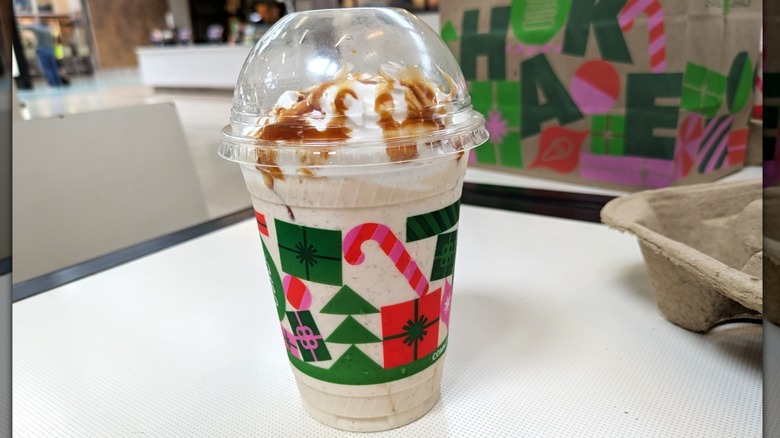 A vanilla custard base milkshake is mixed with sticky toffee pudding. Small chunks are visible in the milkshake itself. There is whipped cream and a caramel toffee sauce drizzled on top.