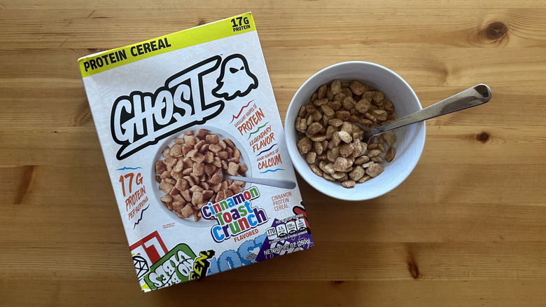 A box of Ghost Cinnamon Toast Crunch cereal with a portion served in a white bowl on a wooden table
