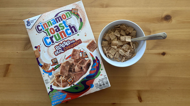 Cinnamon Toast Crunch cereal in white bowl next to a whole box on a wooden table