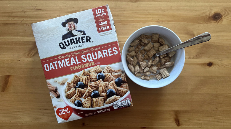 Top view of a box of Quaker Cinnamon Oatmeal Squares cereal with some in a white bowl mixed with milk