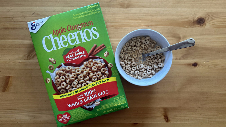 Top view of Cheerios Apple Cinnamon cereal box and a cereal-filled white bowl on table