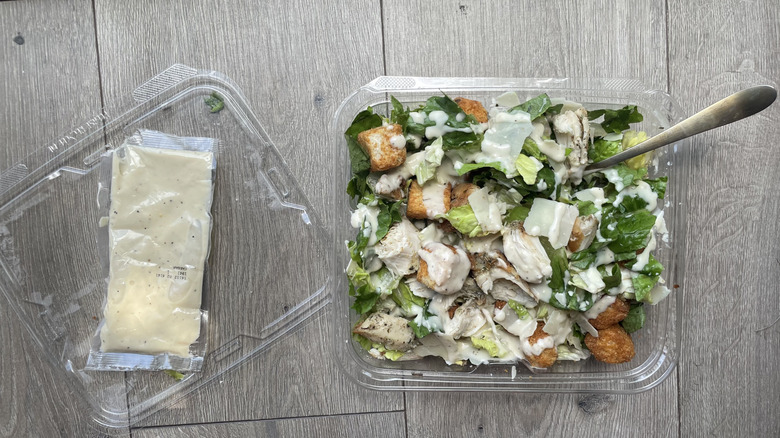 Caesar salad in open container with dressing packet applied