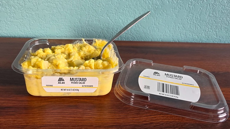 Container of Aldi mustard potato salad open on table with spoon