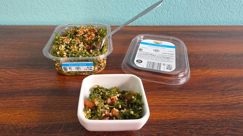 Container of Park Street deli taboule salad open on table with spoon with small white bowl of taboule in front of it