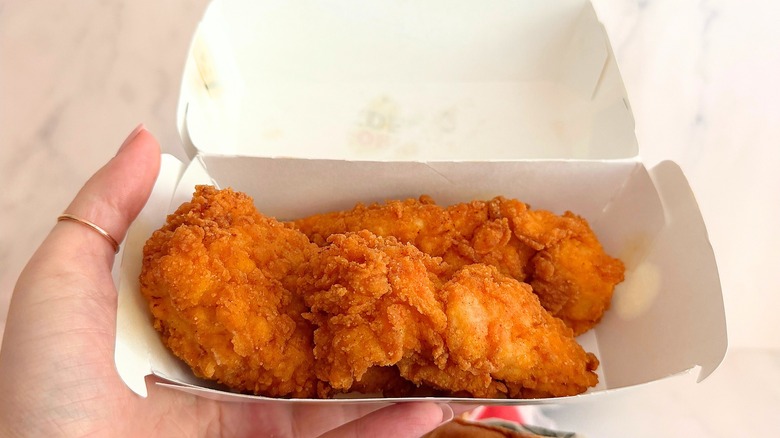 Hand holding Carl's Jr. chicken tenders against white background