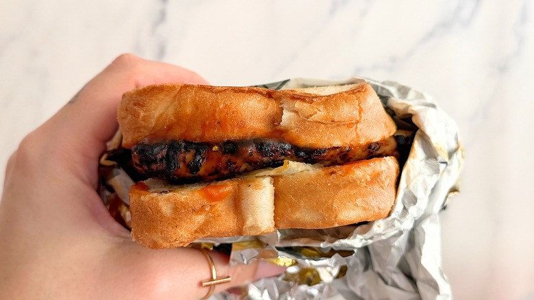 Hand holding Carl's Jr. Charbroiled BBQ Chicken Sandwich against white background
