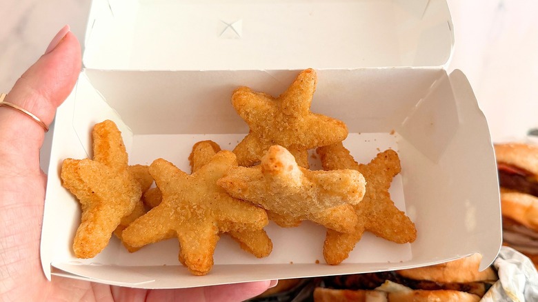 Hand holding box of Carl's Jr. Chicken Stars against white background