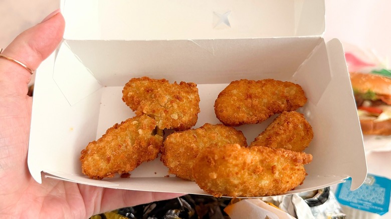 Hand holding box of Carl's Jr. Jalapeño Poppers Bites against white background