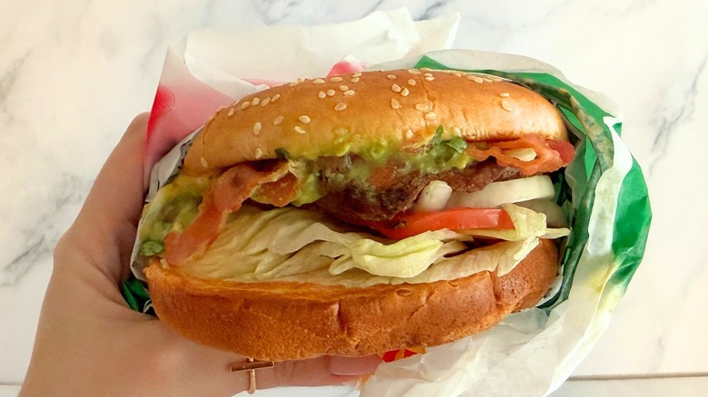 Hand holding Carl's Jr. Single Guacamole Bacon Burger against white background