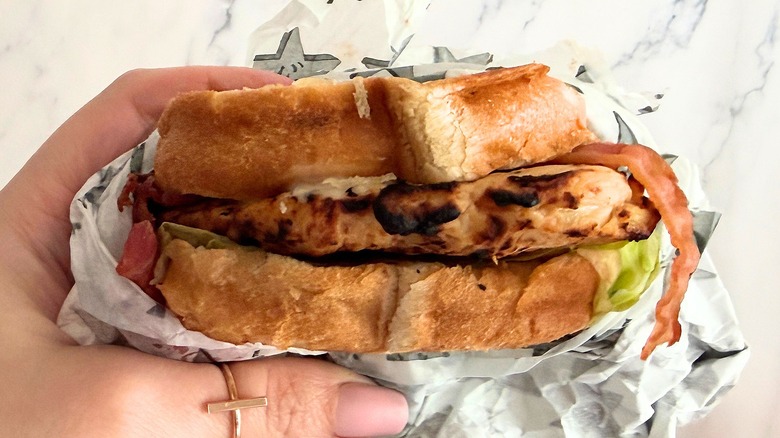 Hand holding Carl's Jr. Charbroiled Chicken Club Sandwich against white background