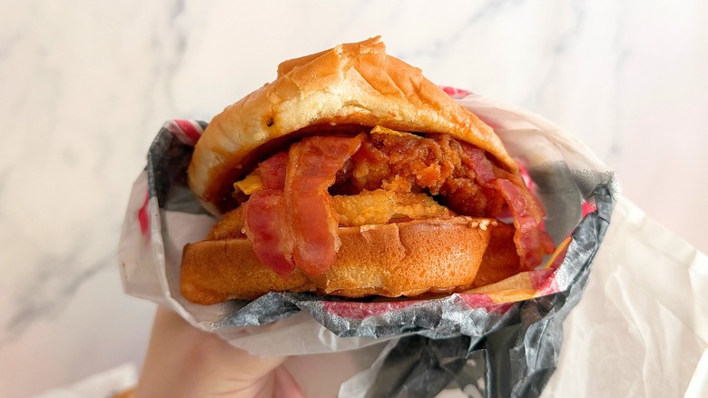 Hand holding Carl's Jr. Western Bacon Chicken Sandwich against white background