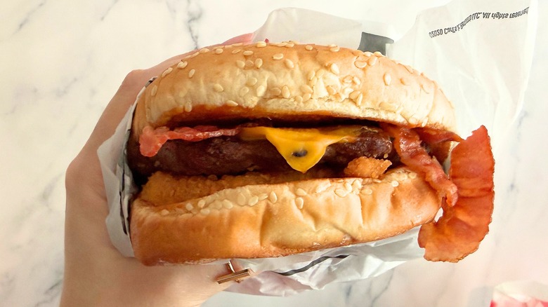 Hand holding Carl's Jr. Single Western Bacon Burger against white background