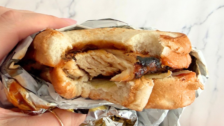 Hand holding Carl's Jr. Charbroiled Chicken Sandwich with bite taken out of it against white background
