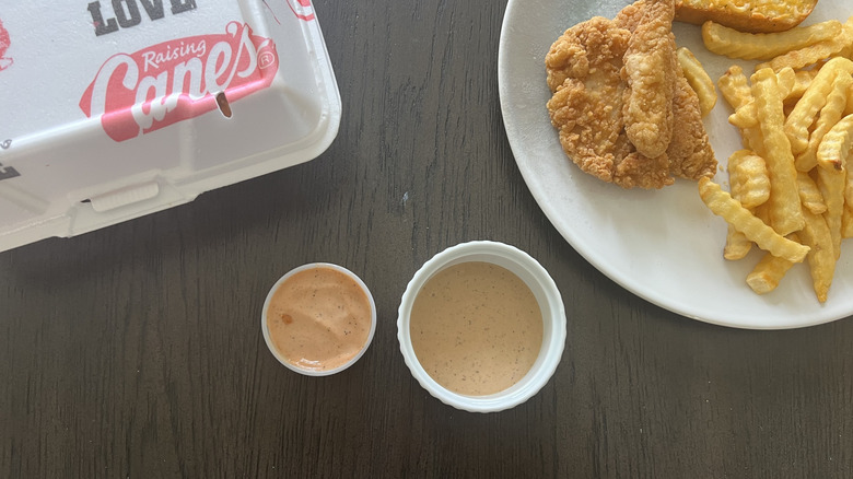 Raising Cane's sauce and Great Value sauce in a dish with takeout and a plate with chicken and fries on the side
