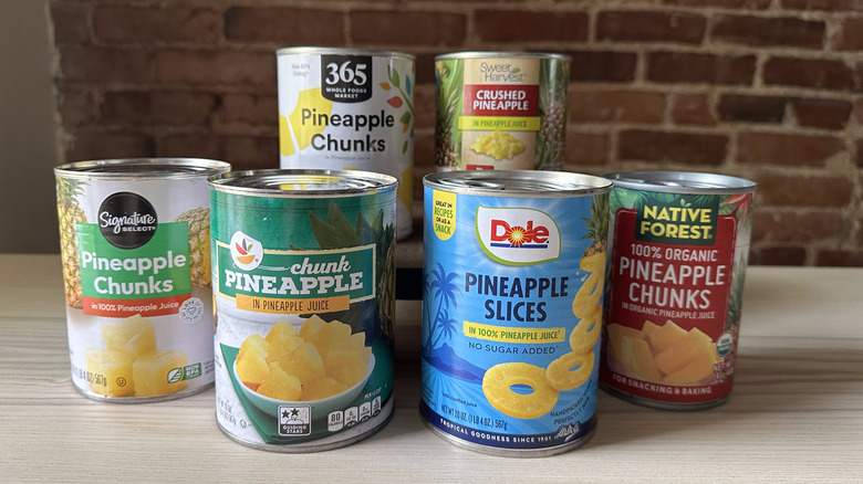 Cans of pineapple on wooden table with brick background