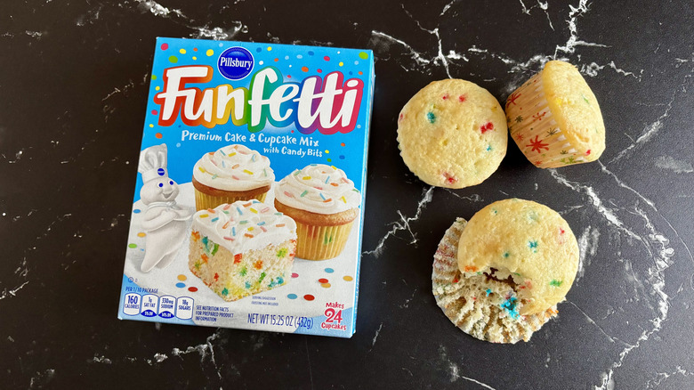 Pillsbury Funfetti cake mix box next to three cupcakes on a marble counter