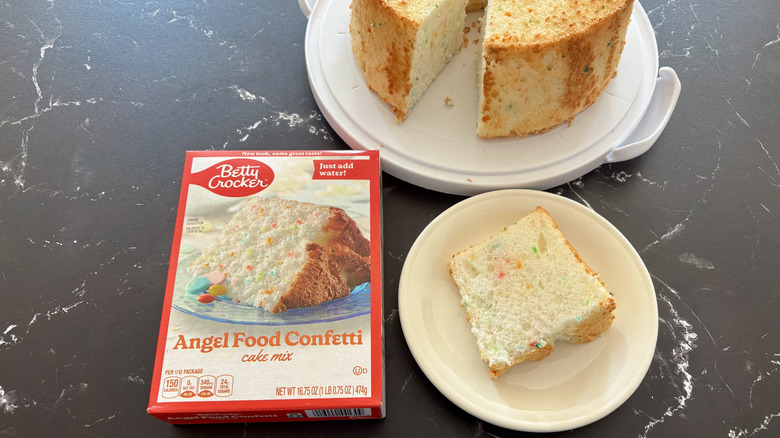 Betty Crocker angel food cake mix box next to cake slice on plate and the entire cake in the back