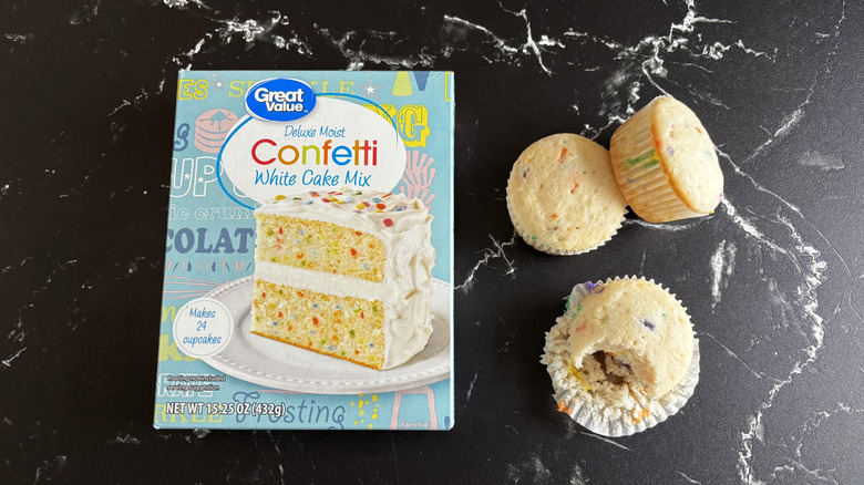 Great Value confetti cake mix box next to three cupcakes with one that was bitten into