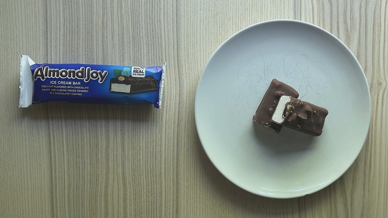Almond Joy Ice Cream Bar sliced and served on a white plate with a wrapper on the side