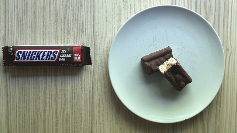 Snickers Ice Cream Bar wrapper with the ice cream bar sliced in half and served on a white plate