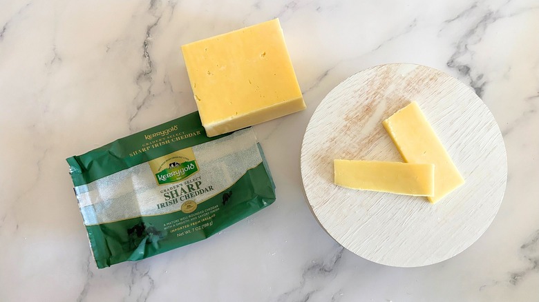 Block of Kerrygold Sharp Irish Cheddar next to packaging and cheese slices on marble surface